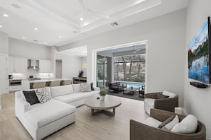 A modern living room with a sectional sofa, a coffee table, and a dining area with a pool view.