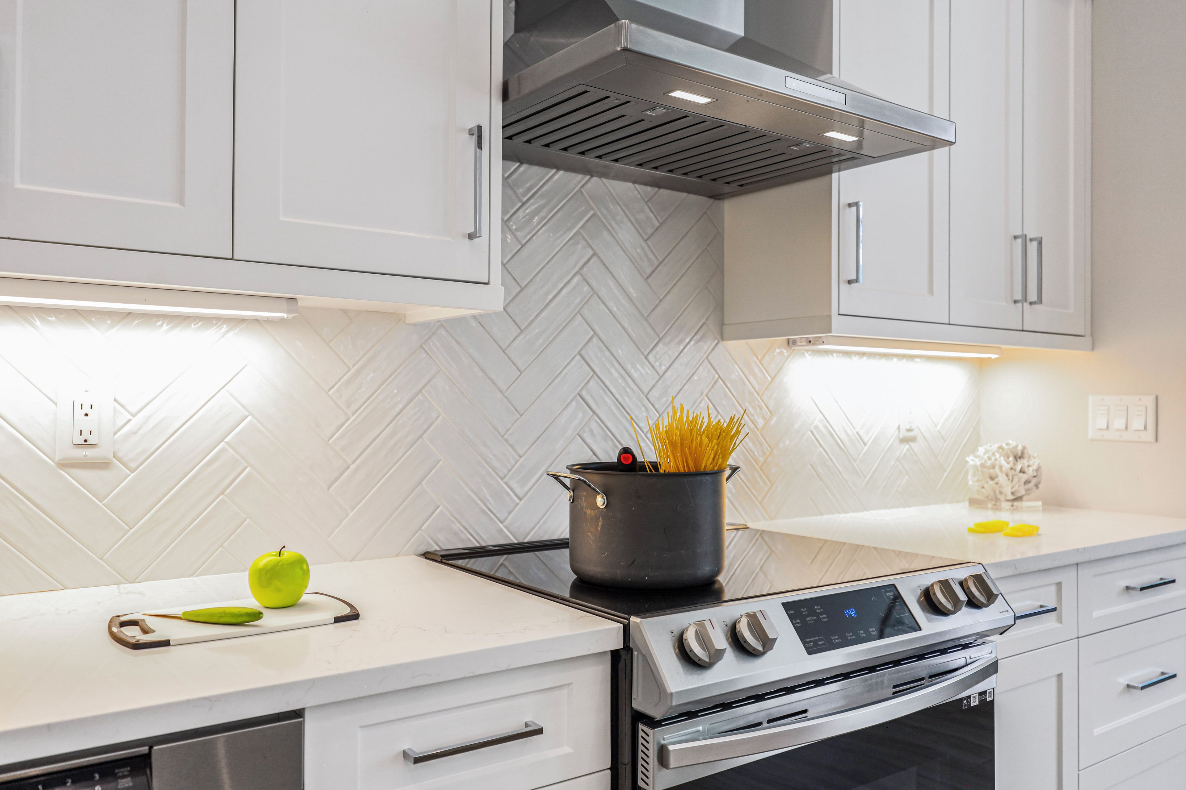 Een moderne keuken met witte kasten, een roestvrijstalen fornuis en een backsplash met een mozaïekpatroon.