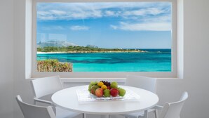 A dining table with a fruit bowl and a view of a turquoise sea and a distant mountain through a large window.