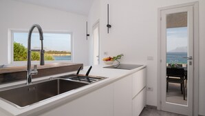 A modern kitchen with a large island, stainless steel sink, and a view of the sea.