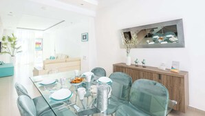 Zona menjador moderna amb taula de vidre, cadires verdes i un armari de fusta amb objectes decoratius.