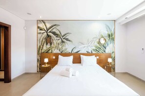 Hotelkamer met een groot bed, een houten hoofdbord, twee nachtkastjes met lampen, en een muurschildering met tropische motieven.