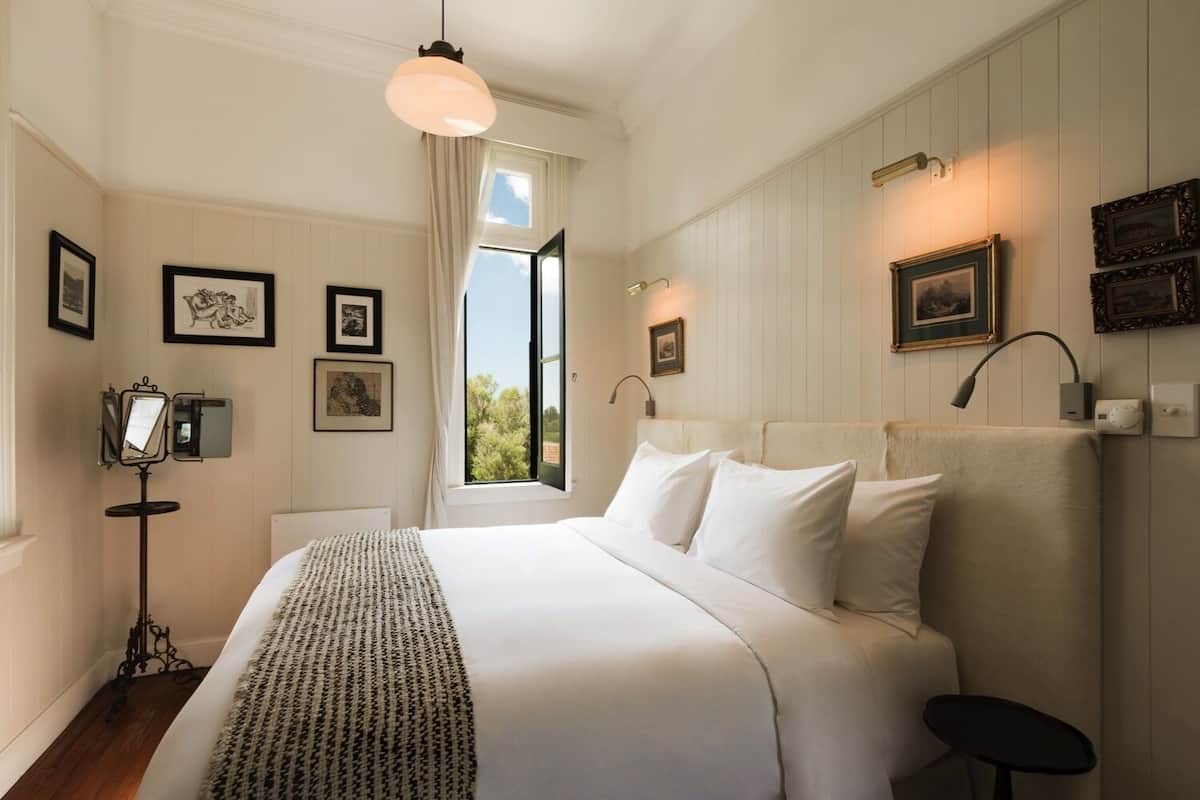 A neatly arranged bedroom with a large bed, a bedside table, a floor lamp, and framed pictures on the walls.