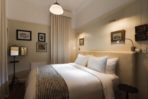 Ein Hotelzimmer mit einem großen Bett, einem Nachttisch, einer Stehlampe und gerahmten Kunstwerken an den Wänden.