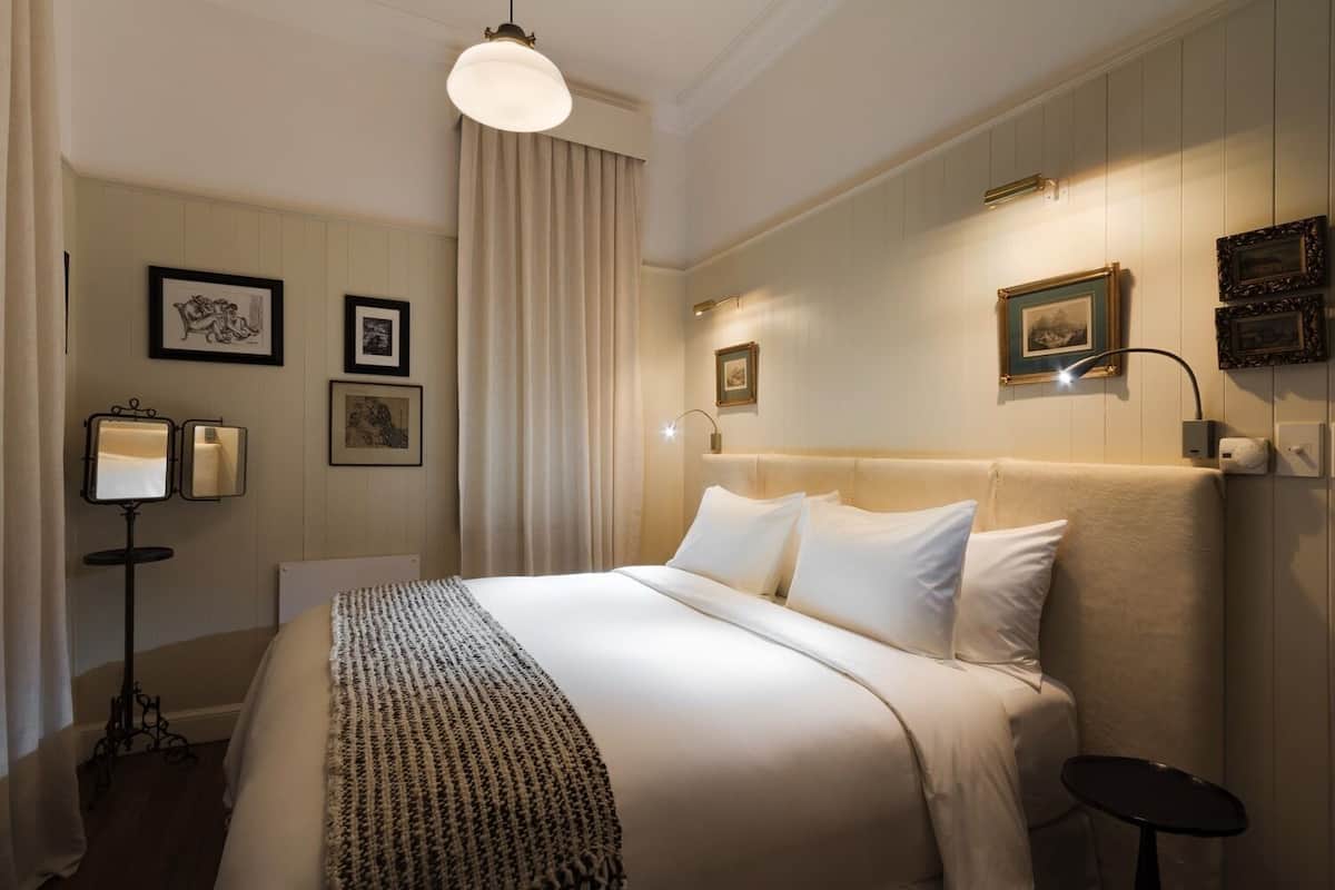 A hotel room with a large bed, a bedside table, a floor lamp, and wall-mounted picture frames.