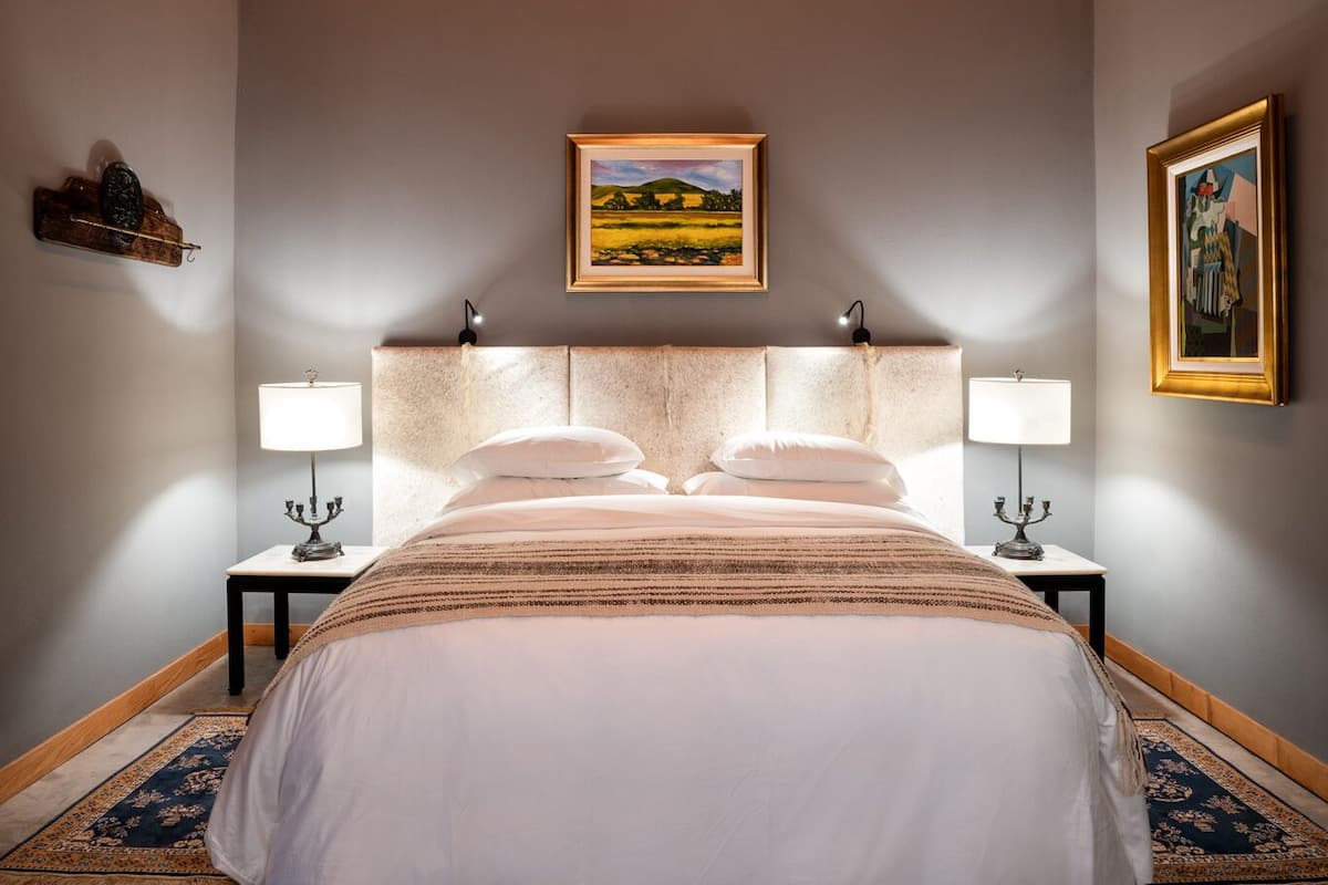 A bedroom with a large bed, two bedside tables with lamps, a headboard, and a wooden ceiling.