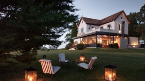Una casa moderna con un amplio frente de cristal, zona de estar exterior con sillas y faroles, y un césped bien cuidado.