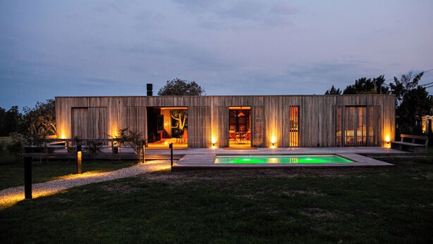 Una casa moderna de madera con diseño de planta abierta, piscina y mobiliario exterior.