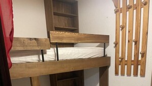 Un lit superposé à deux niveaux, avec une tête de lit en bois et une étagère fixée au mur.
