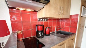Une cuisine compacte avec des carreaux rouges, une plaque de cuisson à induction noire, une machine à café rouge et un évier en acier inoxydable.