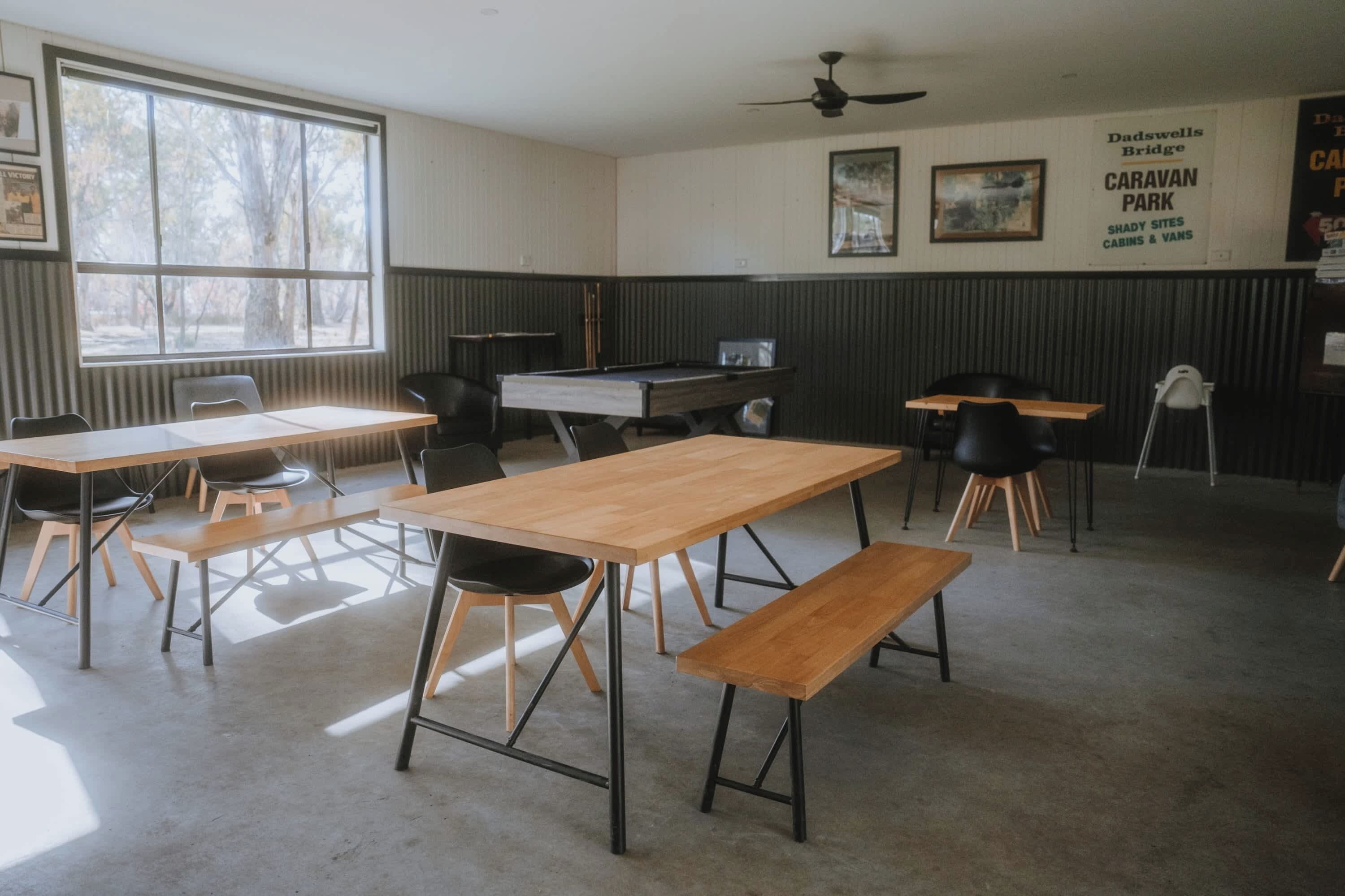 A room with a pool table, several chairs, a bench, and a ceiling fan. There are framed pictures on the wall and a sign mentioning Dadswells Bridge Caravan Park.