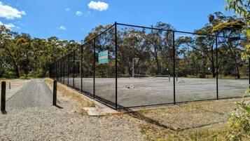 A fenced tennis court with a sign indicating it is a public facility.
