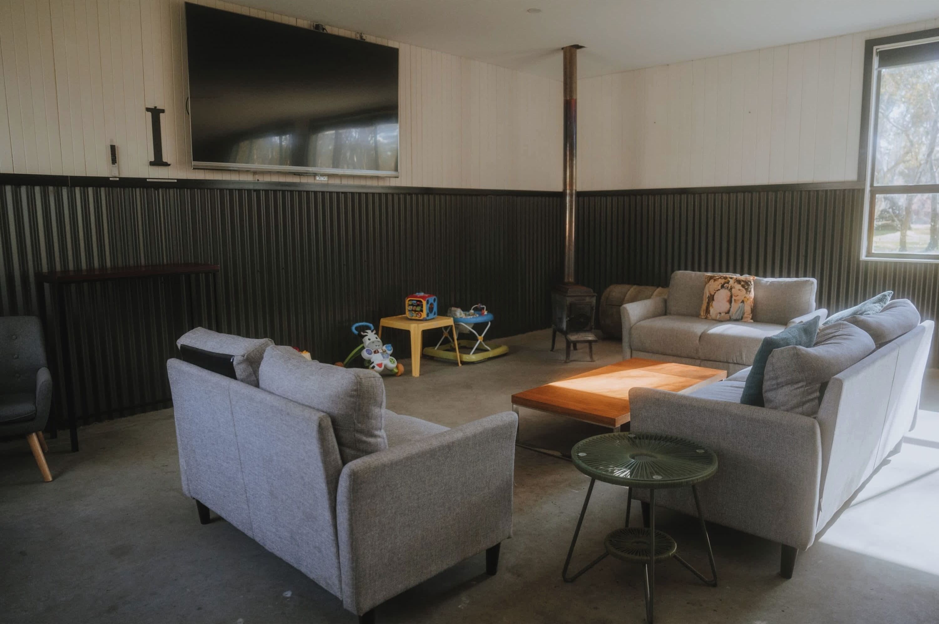 Una sala de estar con dos sofás grises, una mesa de centro de madera, una mesita auxiliar, un televisor y un ventanal grande.