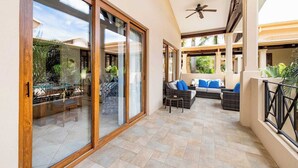Un patio techado con mobiliario exterior, ventilador de techo y vistas del paisaje circundante.