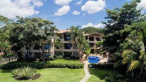 Un hotel de varios pisos con piscina, rodeado de exuberante vegetación y palmeras.