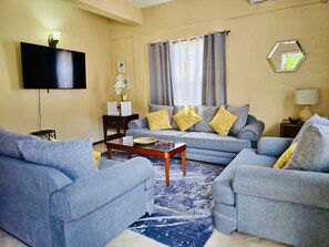 A living room with a sofa set, a coffee table, a flat-screen TV, and a lamp. - Soufrière, St. Lucia 2BR Near Pitons Town Center Spacious + WiFi (Soufriere)