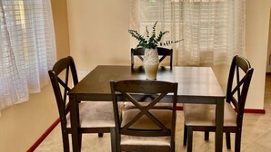 A dining area with a table, four chairs, a vase with a plant, and sheer curtains. - Soufrière, St. Lucia 2BR Near Pitons Town Center Spacious + WiFi (Soufriere)