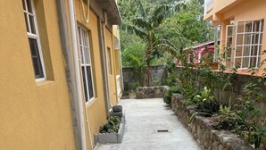 A narrow concrete pathway flanked by buildings with stone walls and small planters with plants. - Soufrière, St. Lucia 2BR Near Pitons Town Center Spacious + WiFi (Soufriere)