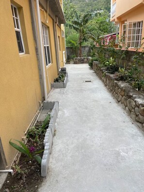 A narrow concrete pathway flanked by buildings with stone walls and small planters with plants. - Soufrière, St. Lucia 2BR Near Pitons Town Center Spacious + WiFi (Soufriere)