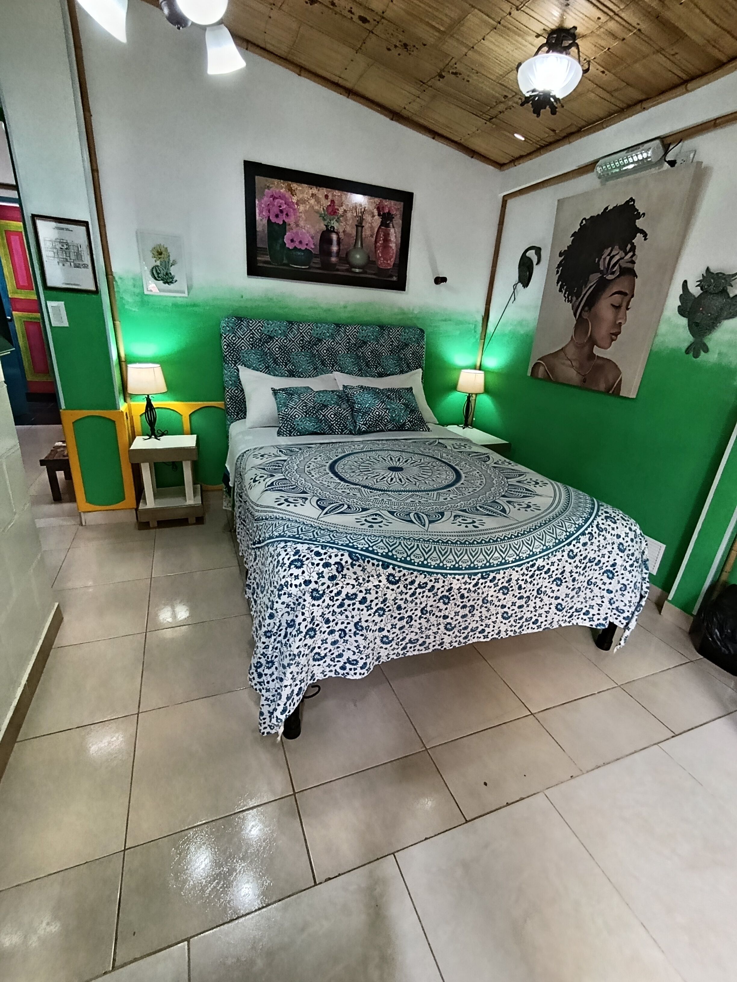 A bedroom with a bed, green walls, a ceiling fan, a framed picture, and a nightstand with a lamp.