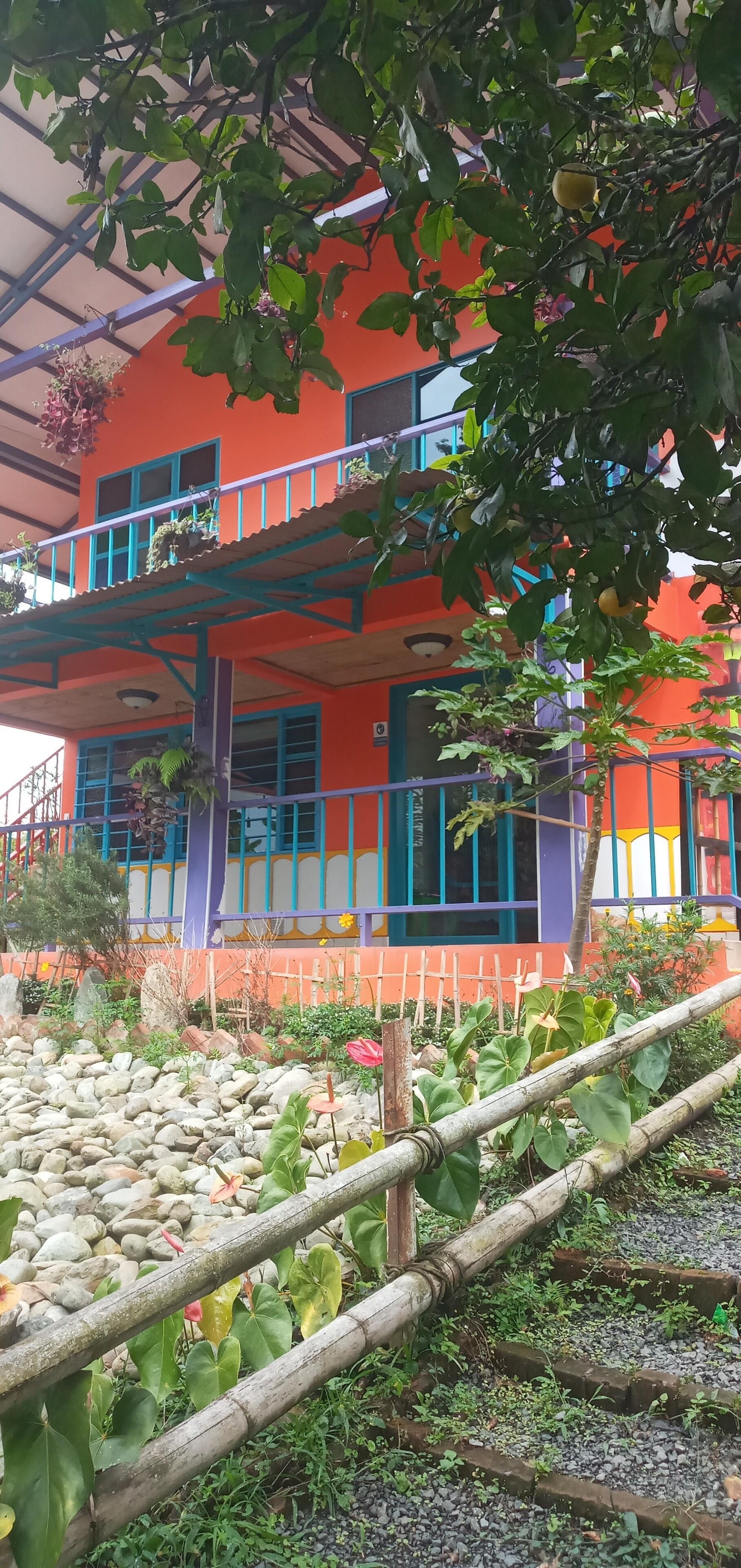 Un edificio de varios pisos con balcones, un jardín con rocas y plantas, y un exterior colorido.