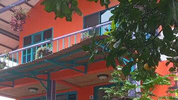 Un edificio de varios pisos con balcones, un jardín con rocas y plantas, y un exterior colorido.