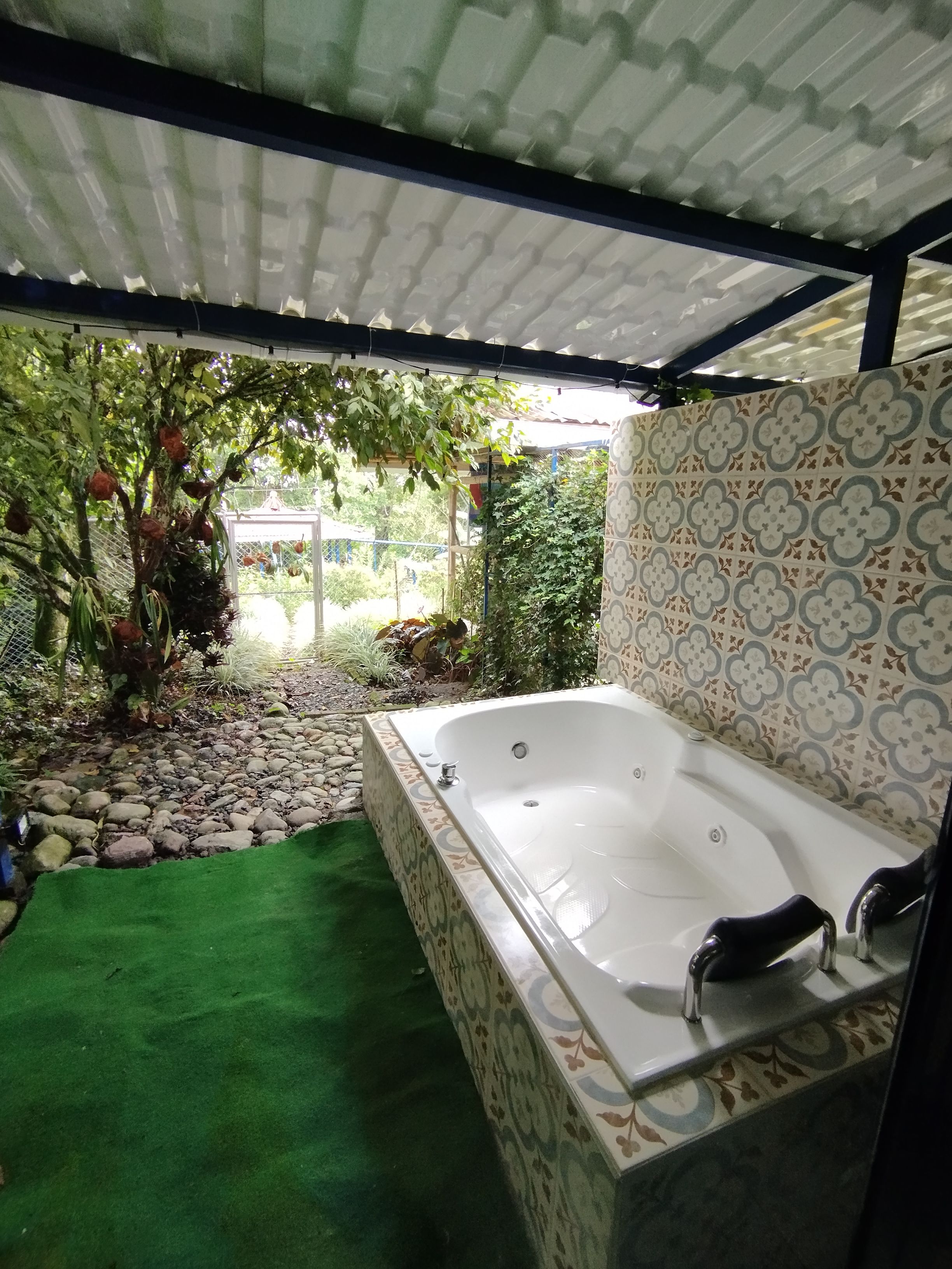 Un área de spa con una bañera grande, césped artificial verde y un revestimiento de pared con azulejos estampados.