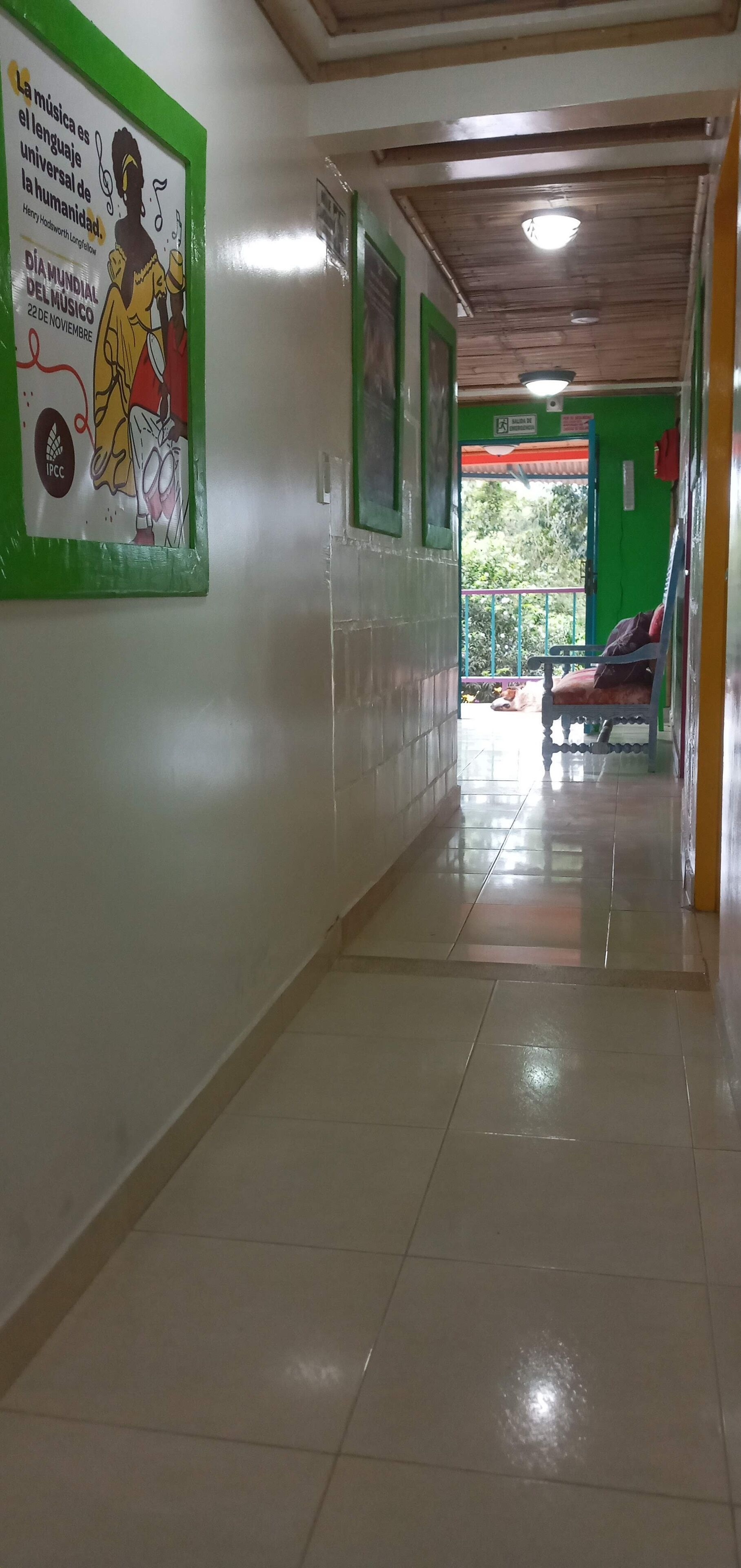 A corridor with tiled floors and green walls, leading to a balcony with a chair and a dog.