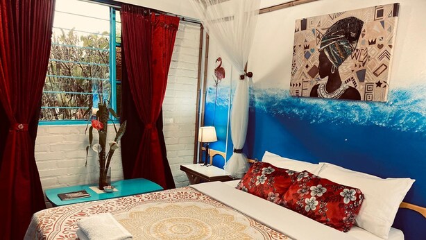 Un dormitorio con cama, mesita de noche, ventana con cortinas, un cuadro en la pared y vistas al exterior.