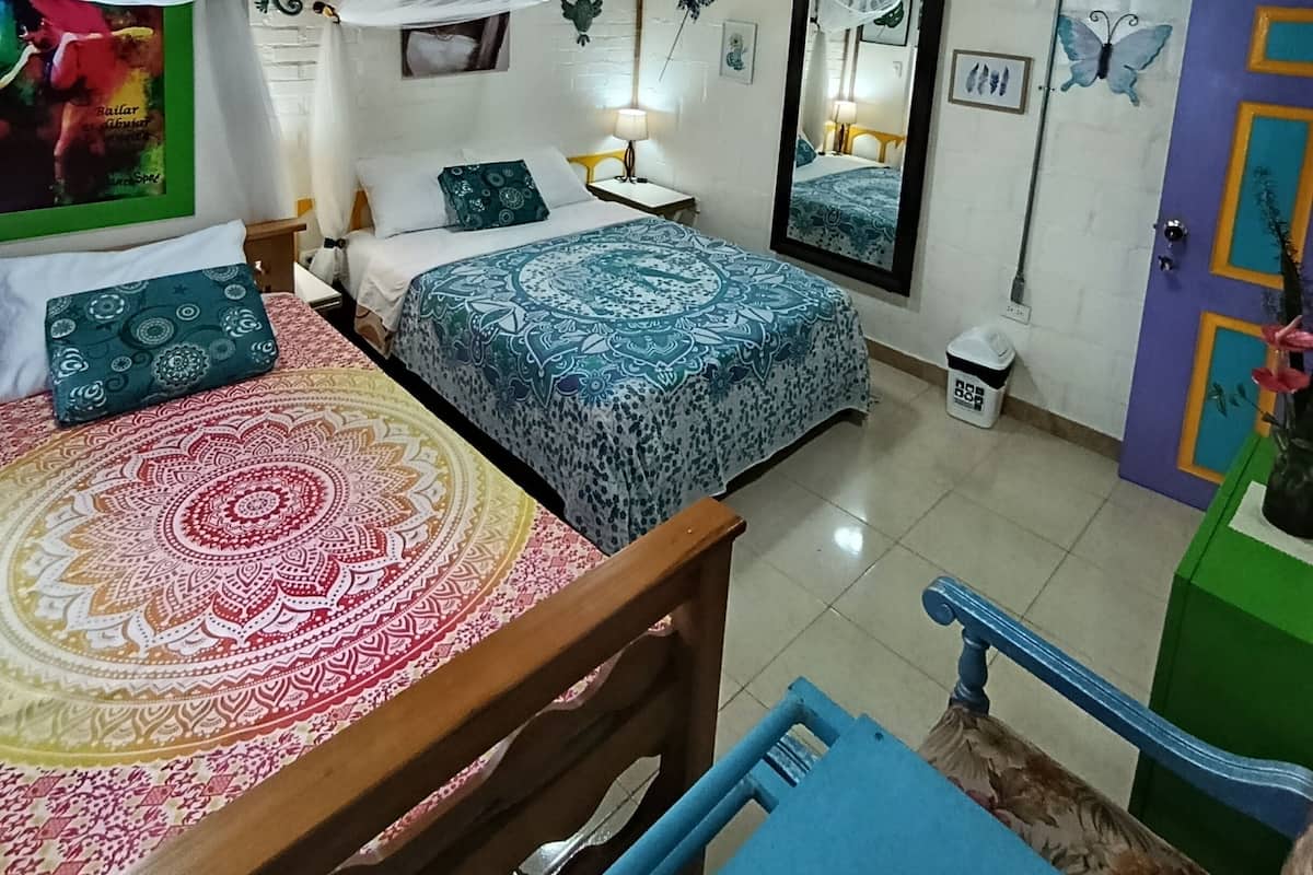 Ein Zimmer mit zwei Betten, einer Holzbalkendecke, einem Spiegel und einem grünen Stuhl.