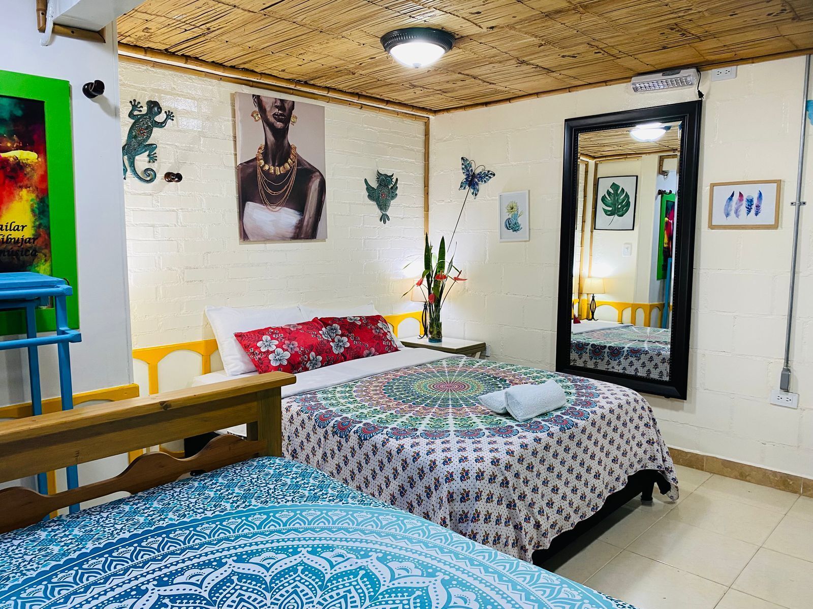 Ein Zimmer mit einem Bett, einer hölzernen Bank, einem Spiegel und einer Wand mit unterschiedlichen Dekorationen.