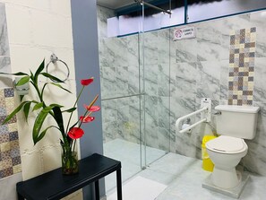 A bathroom with a glass shower enclosure, a toilet, a sink with a towel rack, and a vase with flowers on a black table. - Finca San Miguel Filandia  (Filandia)