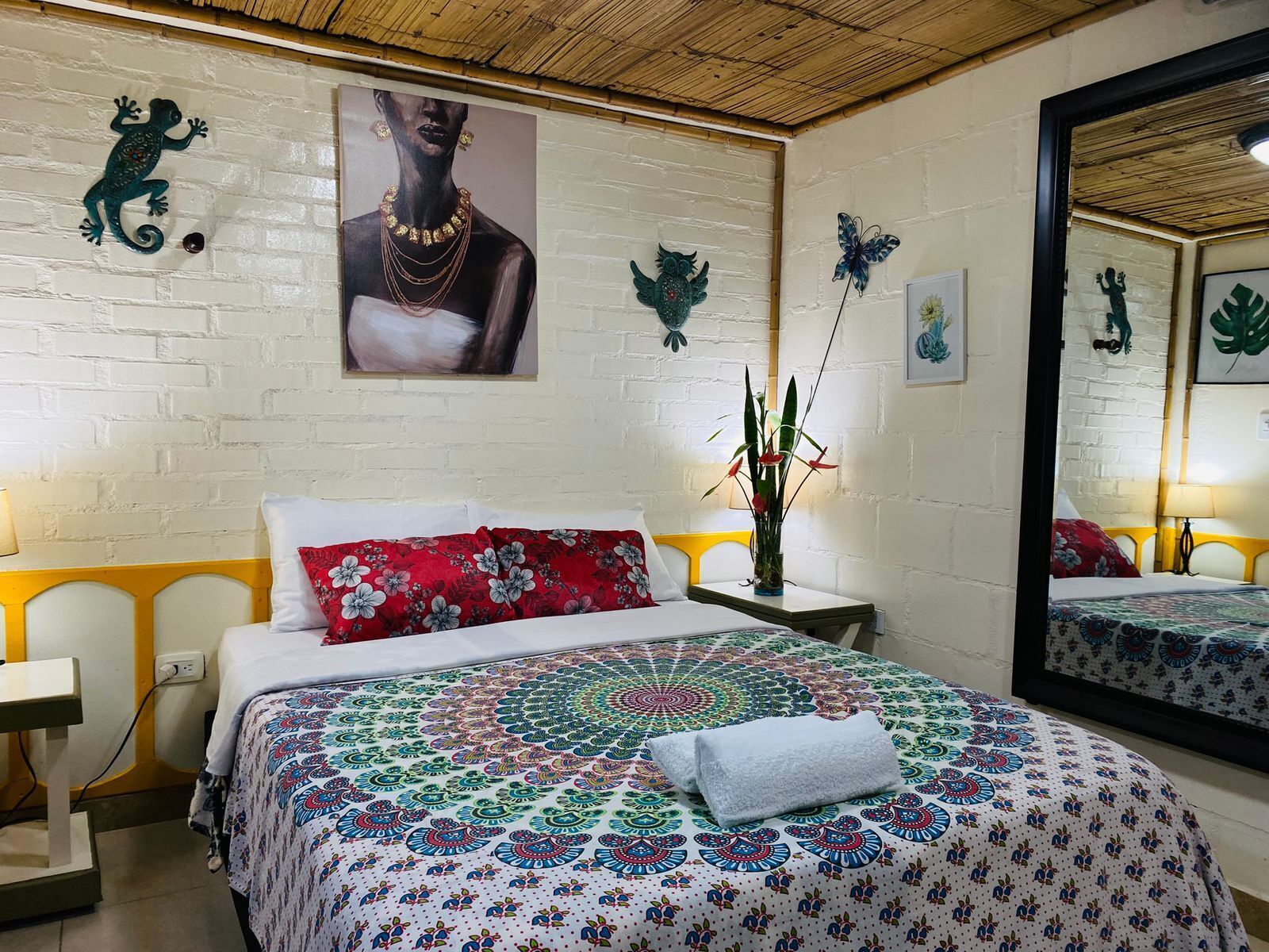 A room with a bed, a nightstand, a mirror, and wall decorations including a lizard, a painting of a woman, and a butterfly.