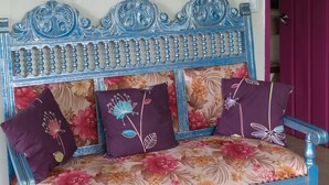 Un sofá azul con tapicería floral y cojines decorativos, ubicado frente a una pared con un cuadro de paisaje tropical.