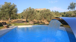 A swimming pool with a waterfall feature, surrounded by trees and a distant building. - Country house, lovingly renovated in the olive grove, large panoramic pool, air conditioning system (Caldana)