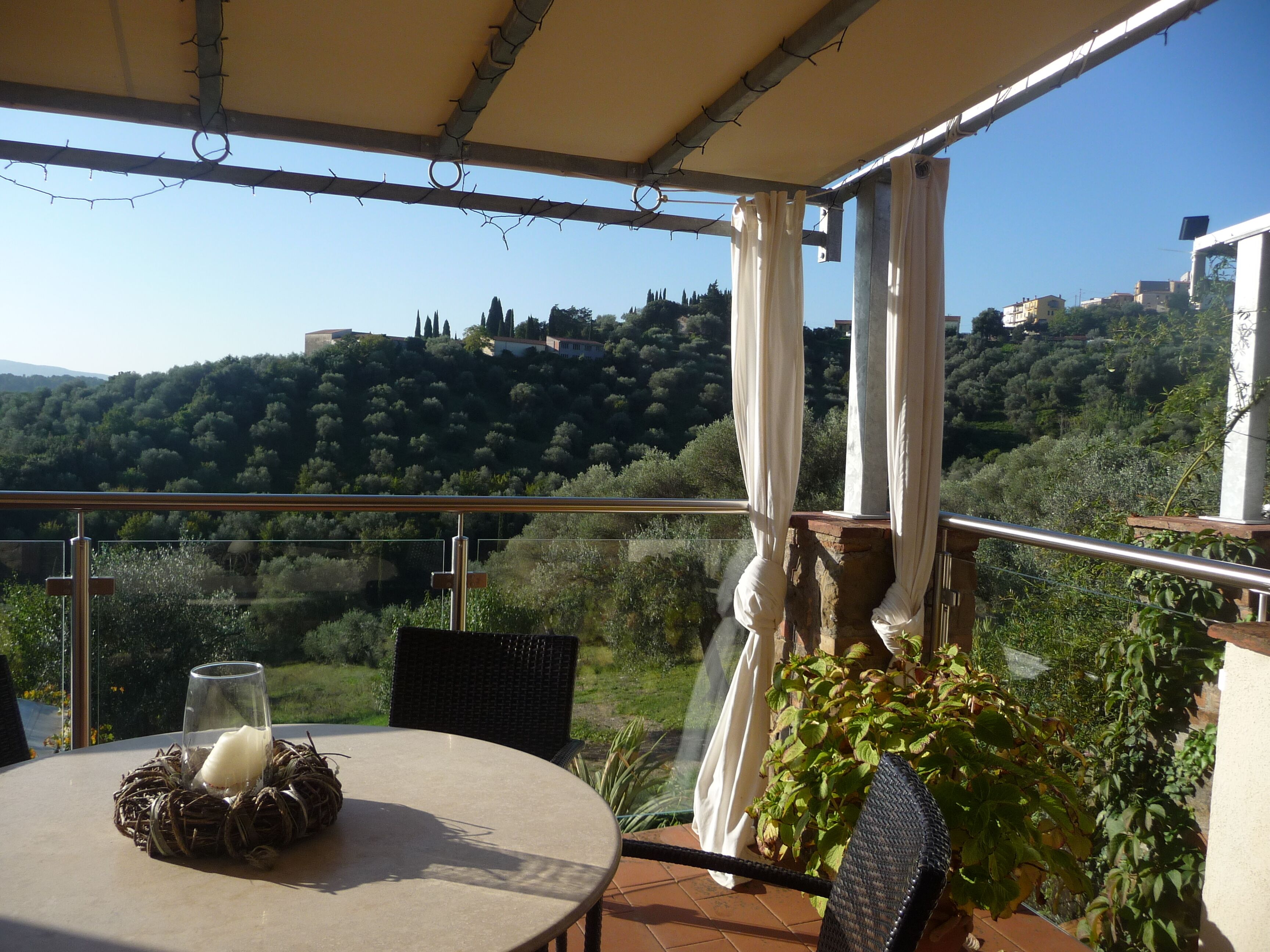 Une terrasse avec une table, des chaises et une vue sur une colline parsemée de bâtiments.