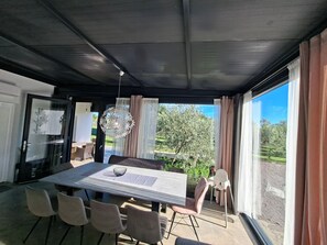 A modern dining area with a table and chairs, a hanging light fixture, and large windows with curtains. - Hacienda MATEA – an oasis of romance near the beaches, Pula (Pula)