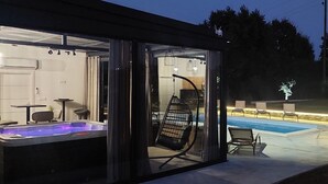Een moderne buitenjacuzzi met glazen omheining, zitplaatsen en een zwembad.