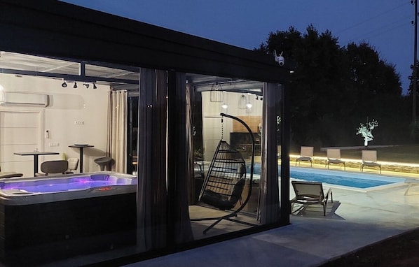 Un espace moderne aménagé à l’extérieur avec un jacuzzi, une structure en verre, des sièges et une piscine.
