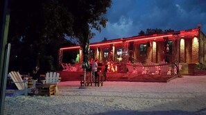 A building with a red-lit exterior, outdoor seating with white chairs, and a gravel ground. - Hacienda MATEA – an oasis of romance near the beaches, Pula (Pula)