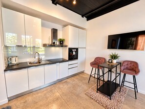 A modern kitchen with white cabinets, a black countertop, and a built-in oven. There is a small table with two chairs and a rug.