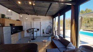Een modern interieur met een keuken, eethoek en zithoek bij een groot raam met uitzicht op een zwembad.