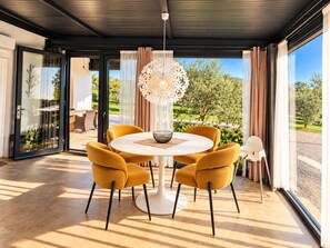 Uma sala de jantar moderna com uma mesa redonda e quatro cadeiras, um lustre decorativo e vista para o verde lá fora.