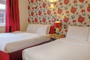 Une chambre d’hôtel avec deux lits, une table de chevet avec une lampe et un papier peint à motifs floraux.
