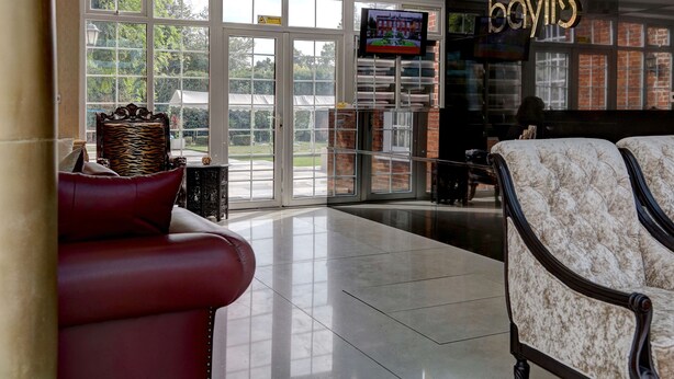 A spacious lobby with a red leather sofa, a patterned armchair, and a television mounted on the wall. - Baylis Park Hotel (Slough)