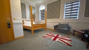 A bedroom with a four-poster bed, a sofa, and a flag rug. - Baylis Park Hotel (Slough)