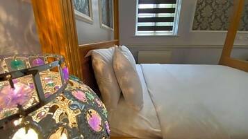 A bed with white linens, a wooden headboard, and a window with blinds.