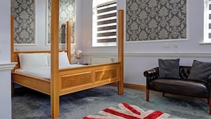 A four-poster bed with a wooden frame and white bedding, a dark leather sofa, and a patterned carpet. - Baylis Park Hotel (Slough)