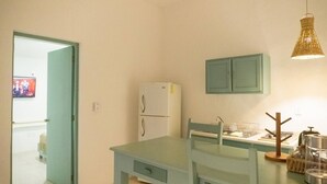 Eine kleine Küche mit Tisch und Stühlen, einem Kühlschrank, einem Schrank und einer Pendelleuchte.