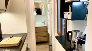 Une cuisine étroite avec un plan de travail noir, une machine à café et une poubelle.